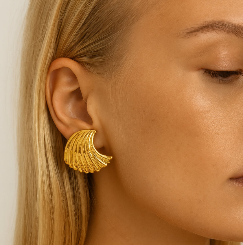 Close-up of a person wearing gold wing-shaped earrings with a neutral background