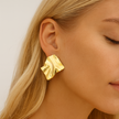Close-up of a person wearing a gold earring with a plain background
