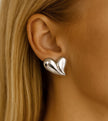 Silver heart-shaped earring worn by a person with blonde hair.