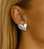Silver heart-shaped earring worn by a person with blonde hair.