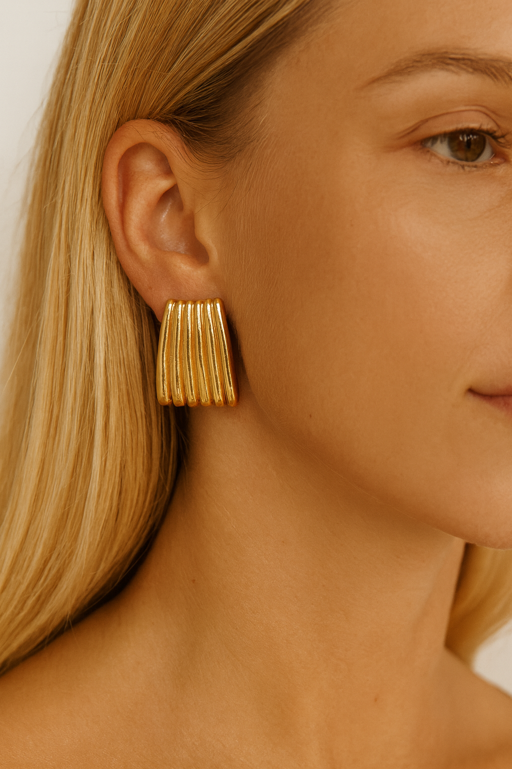 Close-up of a person wearing gold fringe earrings with a neutral background