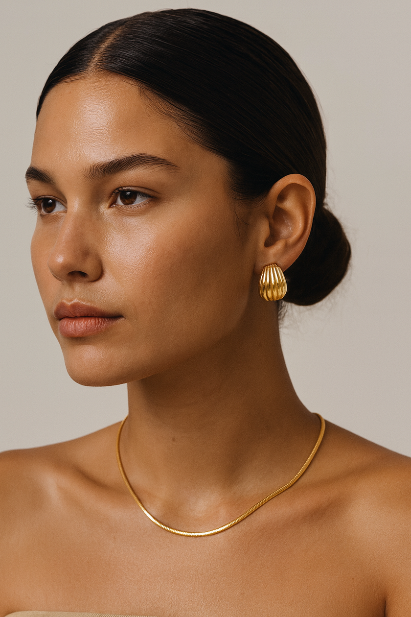 Woman wearing gold earrings and necklace against a neutral background