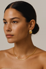 Woman wearing gold earrings and necklace against a neutral background