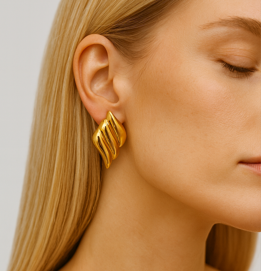 Close-up of a person wearing a gold earring with a plain background