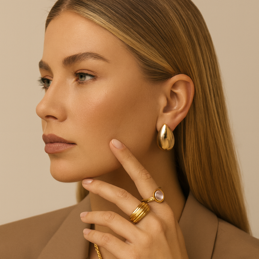 Woman wearing gold earrings and rings against a beige background
