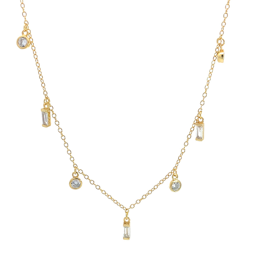 Gold necklace with alternating round and baguette clear gemstone drop pendants on fine chain, white background.