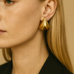 Close-up of a person wearing a gold earring with a neutral background