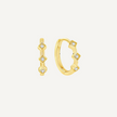 Gold hoop earrings with diamond-like stones on a light beige background