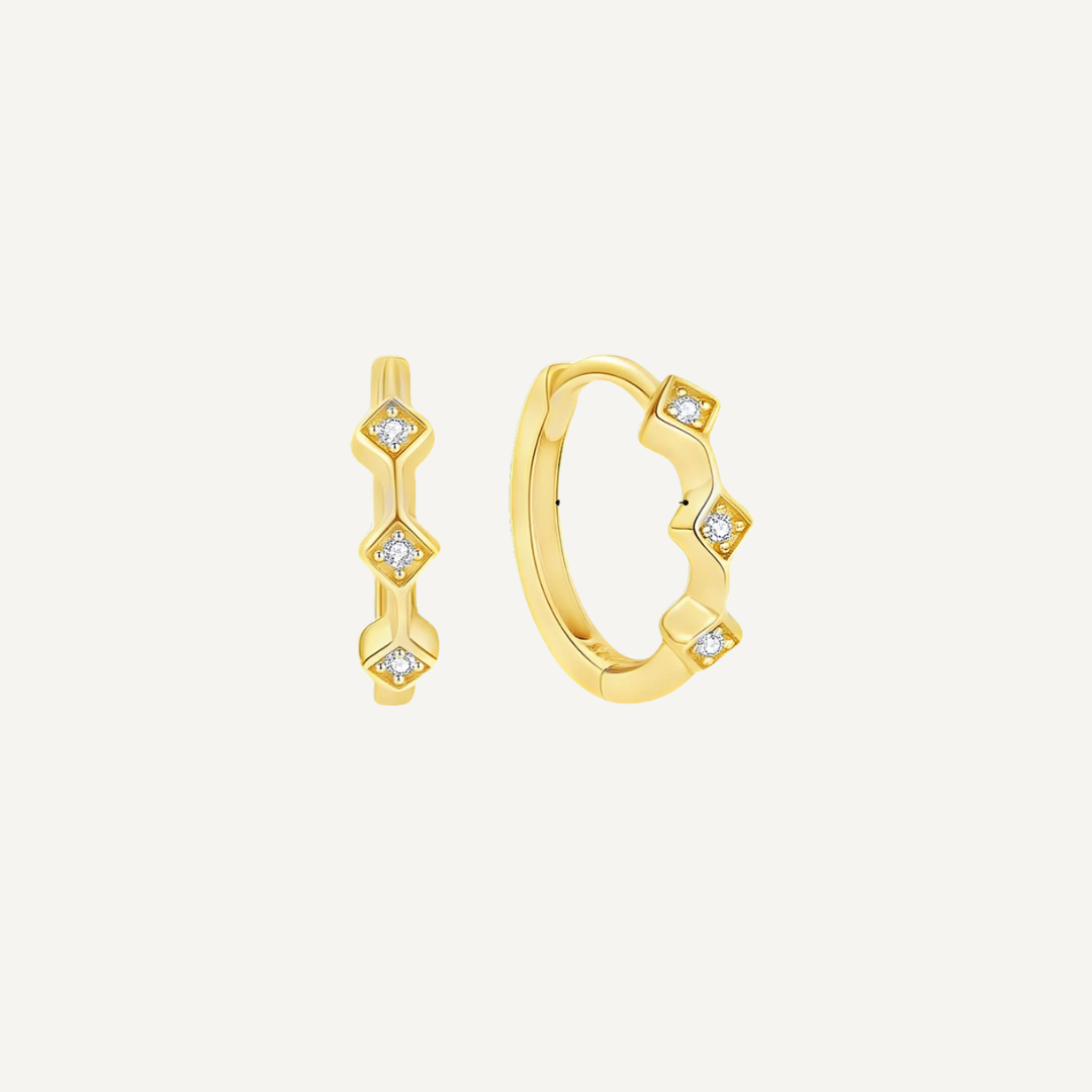 Gold hoop earrings with diamond-like stones on a light beige background