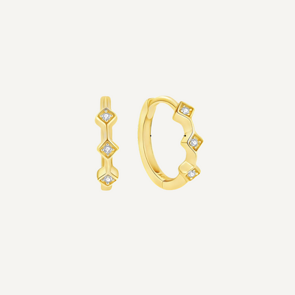 Gold hoop earrings with diamond-like stones on a light beige background
